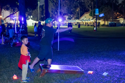 A father and son playing glow-in-the-dark cornhole on the lawn at night