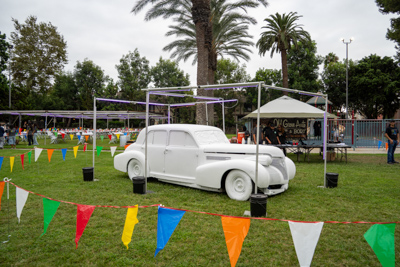 A vintage white classic car on display on the lawn, roped off with colorful pennant flags