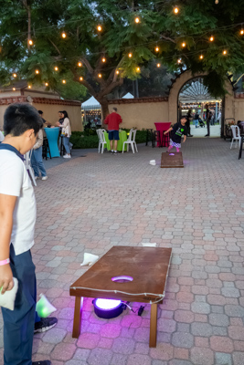 Kids playing cornhole on a glowing board under string lights near a stone archway