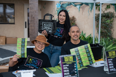 Volunteers at the ticket booth holding up FoGG LIVE tote bags and tasting ticket packs