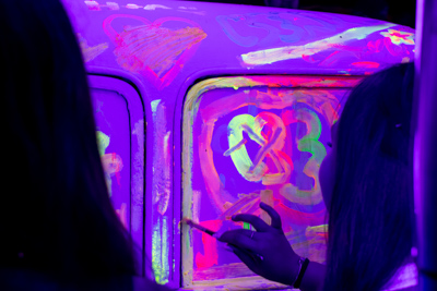 Close-up of hands painting a car with glowing blacklight-reactive paint at Art in the Dark