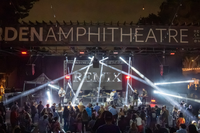 A tribute band performs on the Garden Amphitheatre stage as the crowd dances under crossed spotlight beams