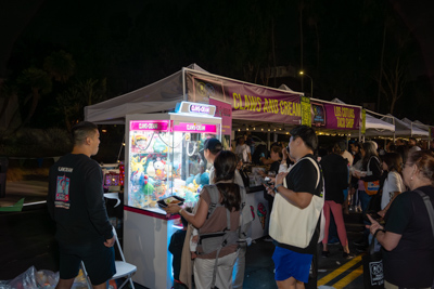 A line of guests waiting at a lit-up ice cream and claw manchine vendor booth at night