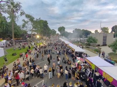 Aerial view of festival-goers filling the street between rows of food vendor tents at dusk