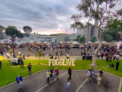 Aerial view of the festival grounds at sunset with a lit-up FOGGLIVE sign on the lawn and rows of vendor tents